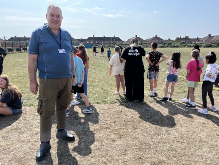 a man, Ian Chambers, standing on a field with a group of young people. The young people have their backs to the camera.