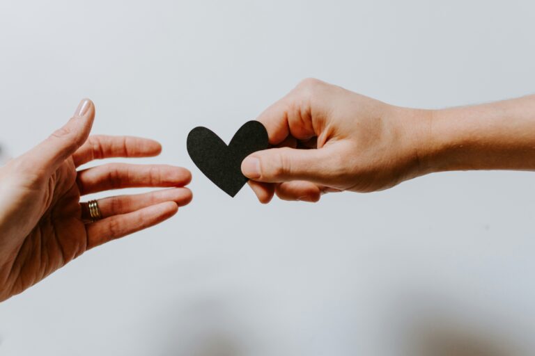 two hands one passing a paper heart to another